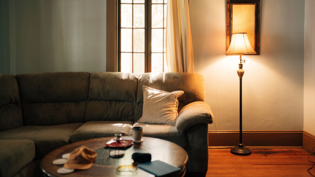 A quiet living room at dusk, a floor lamp glowing beside a worn sofa and a coffee table
